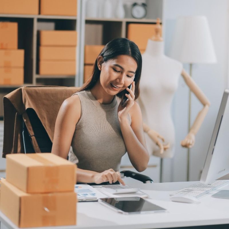 Emprendedora gestionando pedidos de tienda online desde laptop con cajas de envíos.